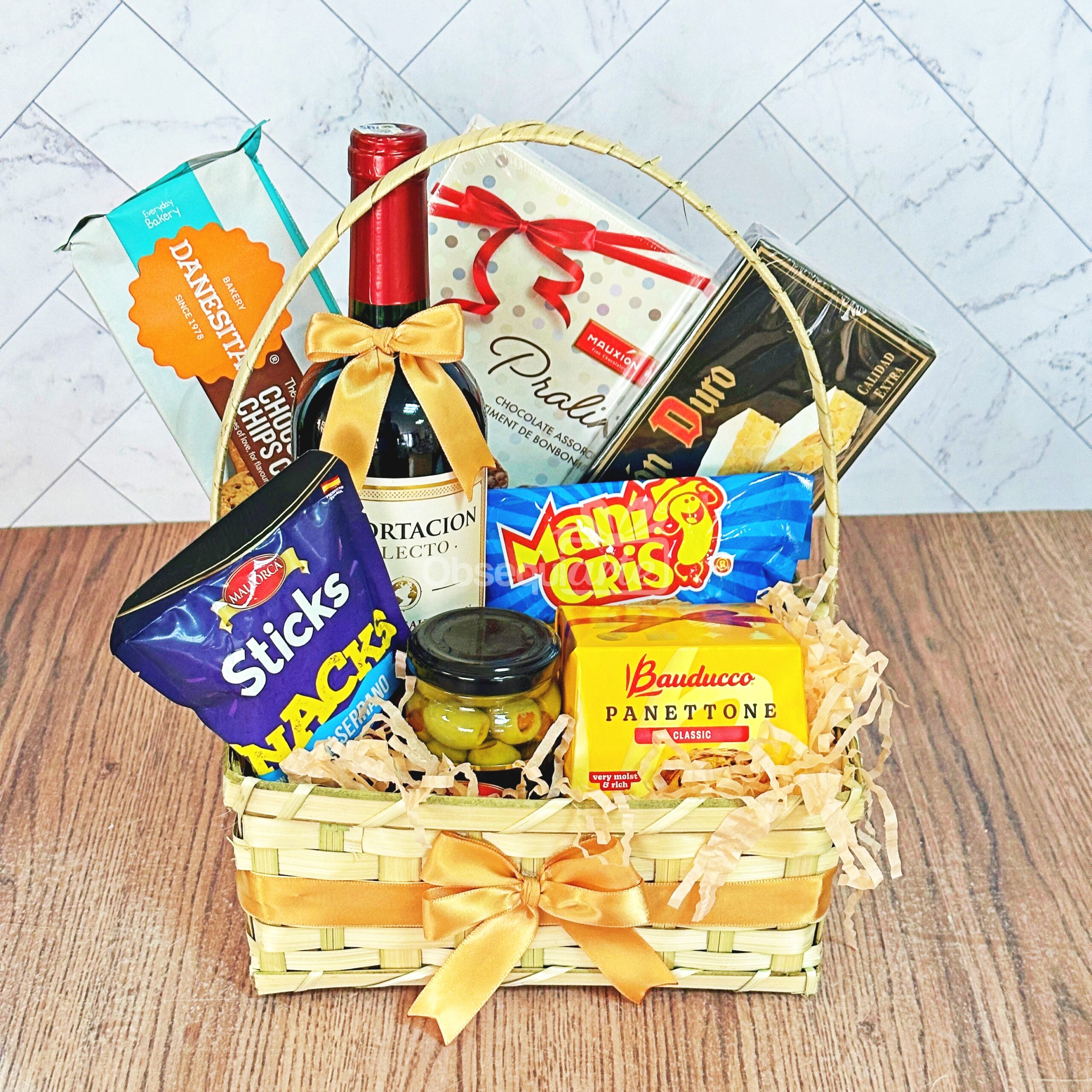 El Regalo Canasta Festiva es una cesta de regalo de mimbre con un lazo amarillo, que contiene vino, galletas, palitos de pan, aceitunas, barquillos, galletas saladas y un pequeño panettone artísticamente dispuestos sobre papel picado.