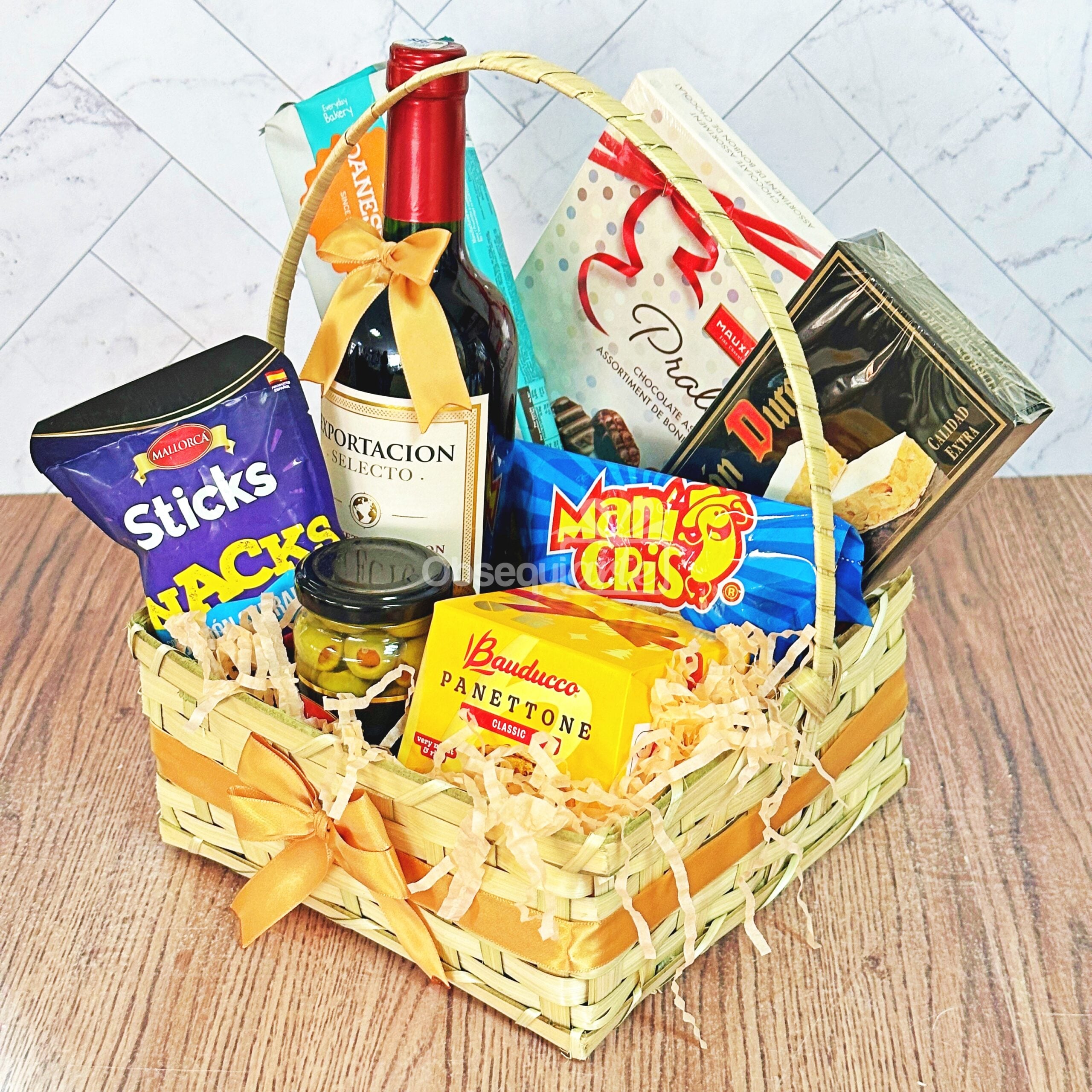 Regalo Canasta Festiva es una cesta de regalo de mimbre con aperitivos variados, vino, palitos de pan, galletas, crackers y panettone, todo ello bellamente decorado con lazos de cinta amarilla.