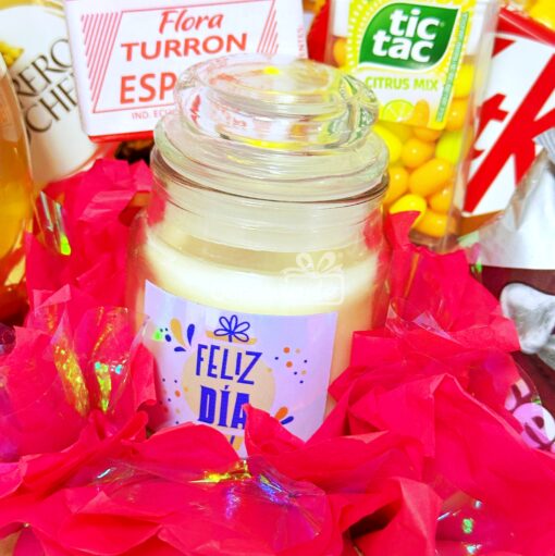 Canasta de regalo denominada "Regalo Primavera con Vela y Vino" con una vela "Feliz Día", arreglada con papel de seda rojo, complementada con dulces Tic Tac, Flora Turrón y una barra de Kit Kat.