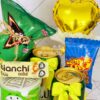 El Regalo Fiesta es una colección festiva de refrigerios que incluyen papas fritas, dulces y bebidas, empaquetados con lazos amarillos y acompañados de un pequeño globo amarillo, perfecto para cualquier fiesta o como un regalo atento.