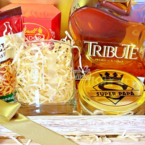 Un majestuoso set de regalo que contiene una botella de Whisky Tribute Premium, una lata de "Super Papá", una vela, chocolate Lindt y un vaso con papel triturado, elegantemente presentado en una caja de madera. El Regalo Royal Guitar perfecto para cualquier ocasión.
