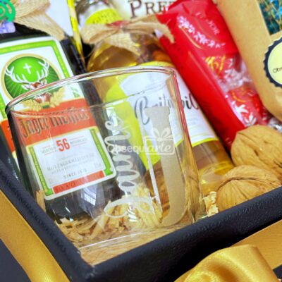 La caja Regalo Élite es un regalo encantador que incluye un vaso, una mini botella de Jägermeister, aperitivos variados y un artículo envuelto, todo bellamente dispuesto sobre un fondo amarillo vibrante. Es perfecta para quienes disfrutan de los pequeños placeres de la vida.