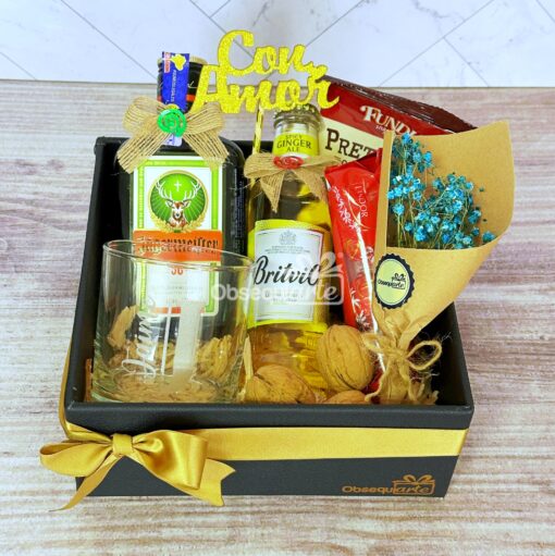 Caja Regalo Élite: Una elegante caja de regalo que incluye whisky, ginger ale, un vaso, bocadillos envueltos, flores azules y un cartel de "Con Amor", todo bellamente presentado en una caja negra adornada con un lazo dorado.