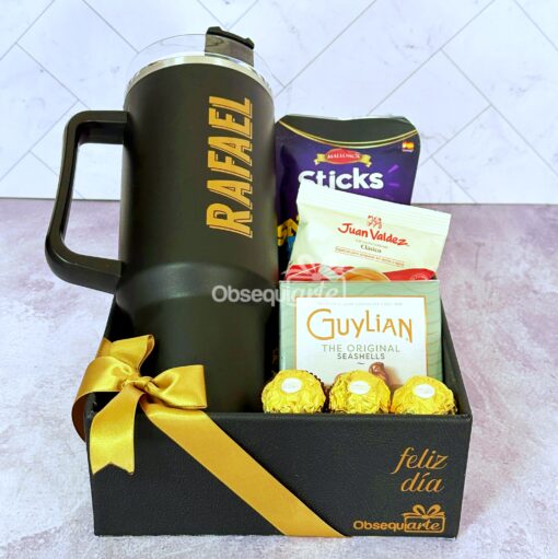 Cesta de regalo con un frasco rotulado "RAFAEL", que contiene patatas fritas, café Juan Valdez, chocolates Guylian y Ferrero Rocher, envuelto con una cinta amarilla y el texto "feliz dia".