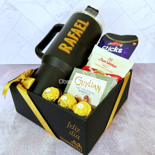 Caja de regalo con frasco grande negro, bombones Ferrero Rocher, bombones Guylian, café Juan Valdez y snack Sticks, con texto "feliz día".