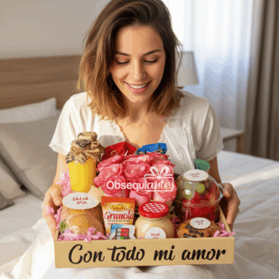 Una mujer sonríe en su cama ante una bandeja de desayuno Desayuno Florido llena de alimentos variados, bebidas y regalos. La bandeja lleva un cartel que dice 