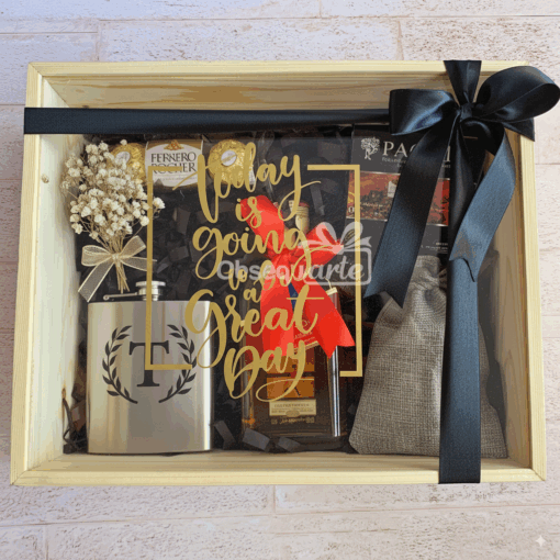 La caja de regalo Regalo Gran Día incluye una petaca de metal, flores secas, bombones, una bolsa gris y una botella en una caja de madera con un lazo negro y un cartel que dice "Hoy va a ser un Gran Día".