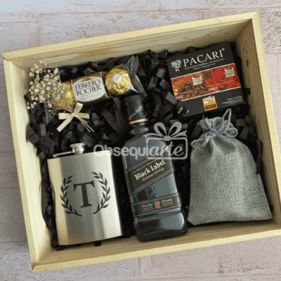 La caja de regalo de madera Regalo Gran Día incluye una petaca de metal, whisky Etiqueta Negra mini, bombones Ferrero Rocher, chocolate Pacari, una bolsa con cordón y flores secas: todo lo que necesita para hacer que cualquier día sea especial.