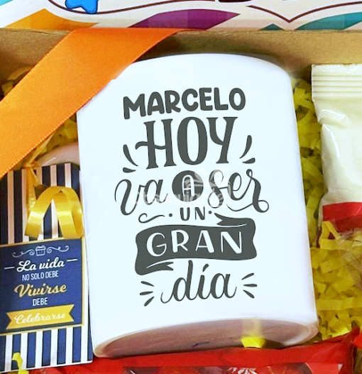 Primer plano de una taza con el texto en español: "Marcelo hoy va a ser un gran día", rodeada de dulces regalos y decoraciones coloridas de la Regalo Sweet Box de Amistad.