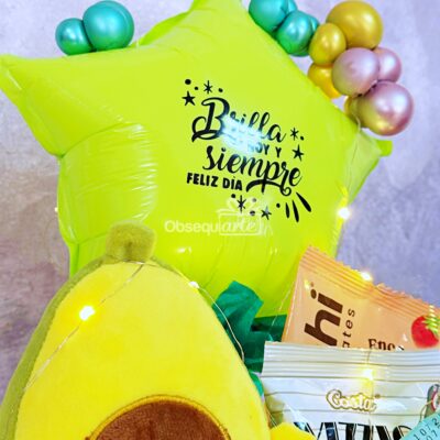 Un globo amarillo en forma de estrella con texto en español, globos de colores, aperitivos, un peluche de aguacate y el Regalo Taza Sopera se unen para una celebración festiva.