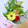 El Ramo de Flores Brisa de Alegría es un ramo vibrante con gerberas amarillas y rojas con flores moradas y amarillas, elegantemente envuelto en papel de seda blanco y presentado en una bolsa rosa de Obsequiarte, que aporta alegría a cualquier espacio.