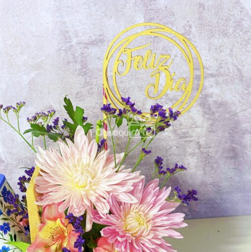 La taza "Regalo con Flores" es un hermoso ramo de flores rosas y blancas con acentos morados y vegetación, que presenta un letrero circular de "Feliz Día", lo que la convierte en el regalo perfecto para cualquier ocasión.