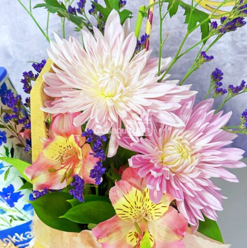 La taza "Regalo Mug con Flores" presenta crisantemos rosados y blancos, alstroemerias amarillas y rosas y ramitas de estátice púrpura sobre un fondo claro: perfecta como un exquisito regalo de flores o para alegrar tu taza favorita.