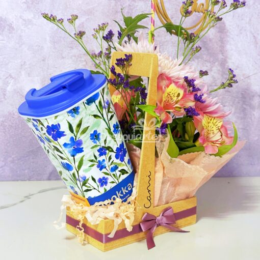 La taza Regalo Mug con Flores, una taza de viaje reutilizable con diseño floral y tapa azul, viene en una caja decorativa con flores variadas y un lazo rosa, perfecta para cualquier ocasión.