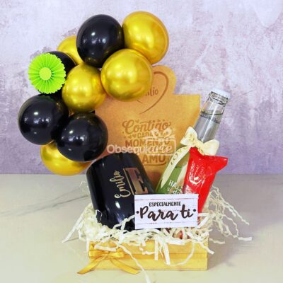 Regalo Galaxy: Canasta de regalo con globos negros y dorados, elegante taza negra, botella de vidrio, artículo envuelto en rojo y letrero “Especialmente Para ti” en papel triturado.