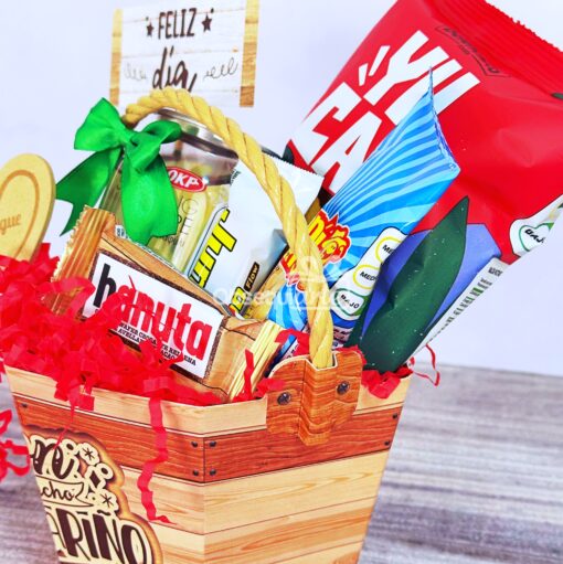 La canasta de regalo está llena de galletas, papas fritas y dulces, decorada con trozos de papel rojo y un cartel de “Feliz día”, lo que la convierte en un regalo ideal para celebrar ocasiones especiales.