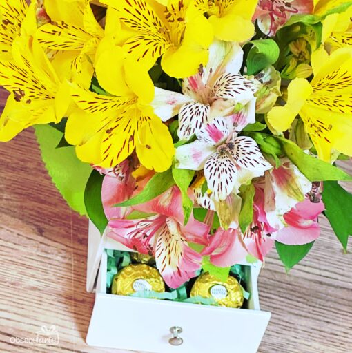 El Regalo Soft con Astromelias presenta un ramo de Astromelias amarillas y rosas en una caja blanca con un cajón que contiene dos bombones Ferrero Rocher envueltos.