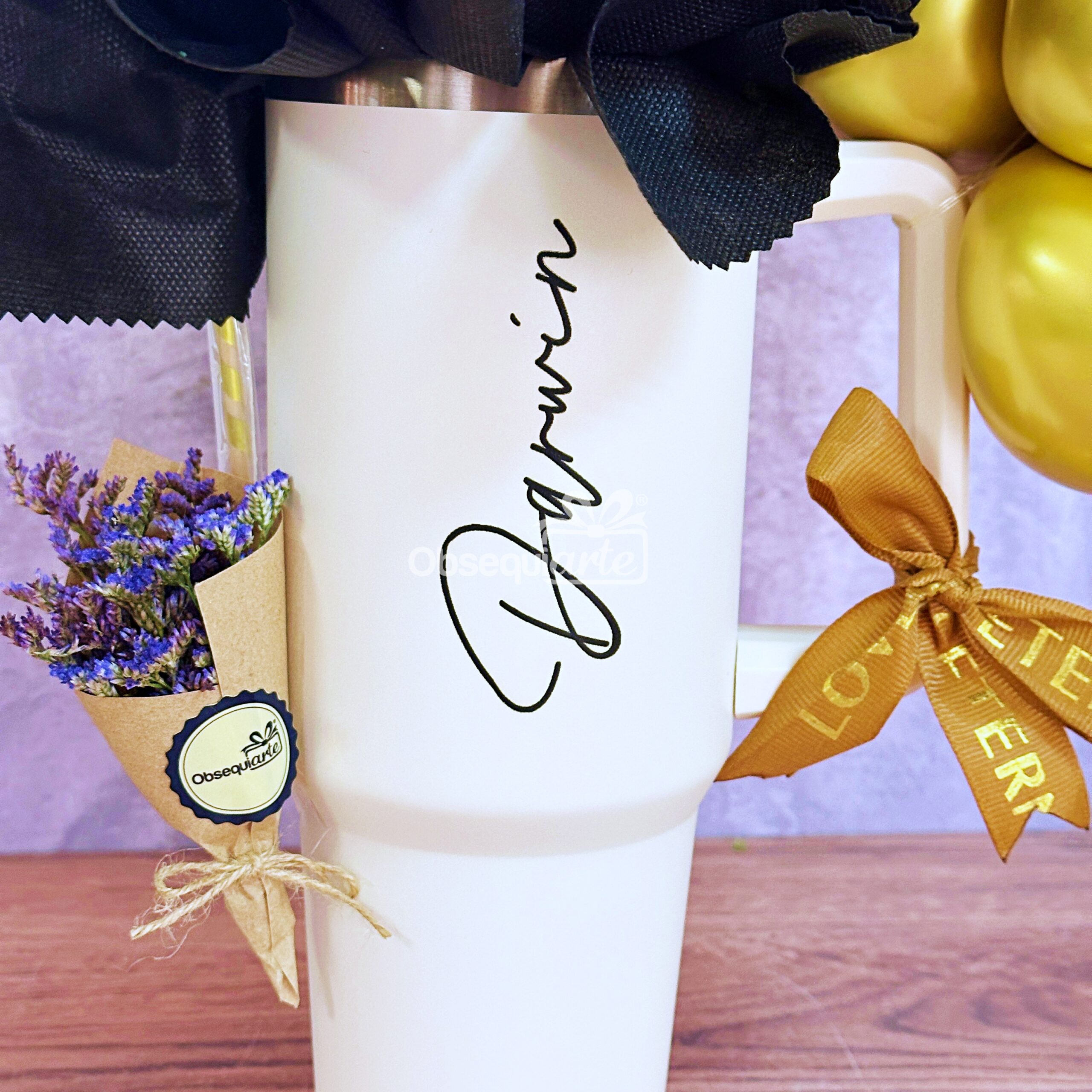 El vaso Regalo Essence para Hombre lleva escrito "Darwin", acentuado con flores moradas y un lazo marrón con texto, creando un regalo considerado y elegante sobre un fondo pastel.