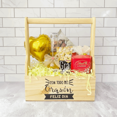 Regalo Jaba Personal: Cesta de madera con aperitivos, un globo de corazón dorado, una bebida, bombones y un lazo. La caja dice 