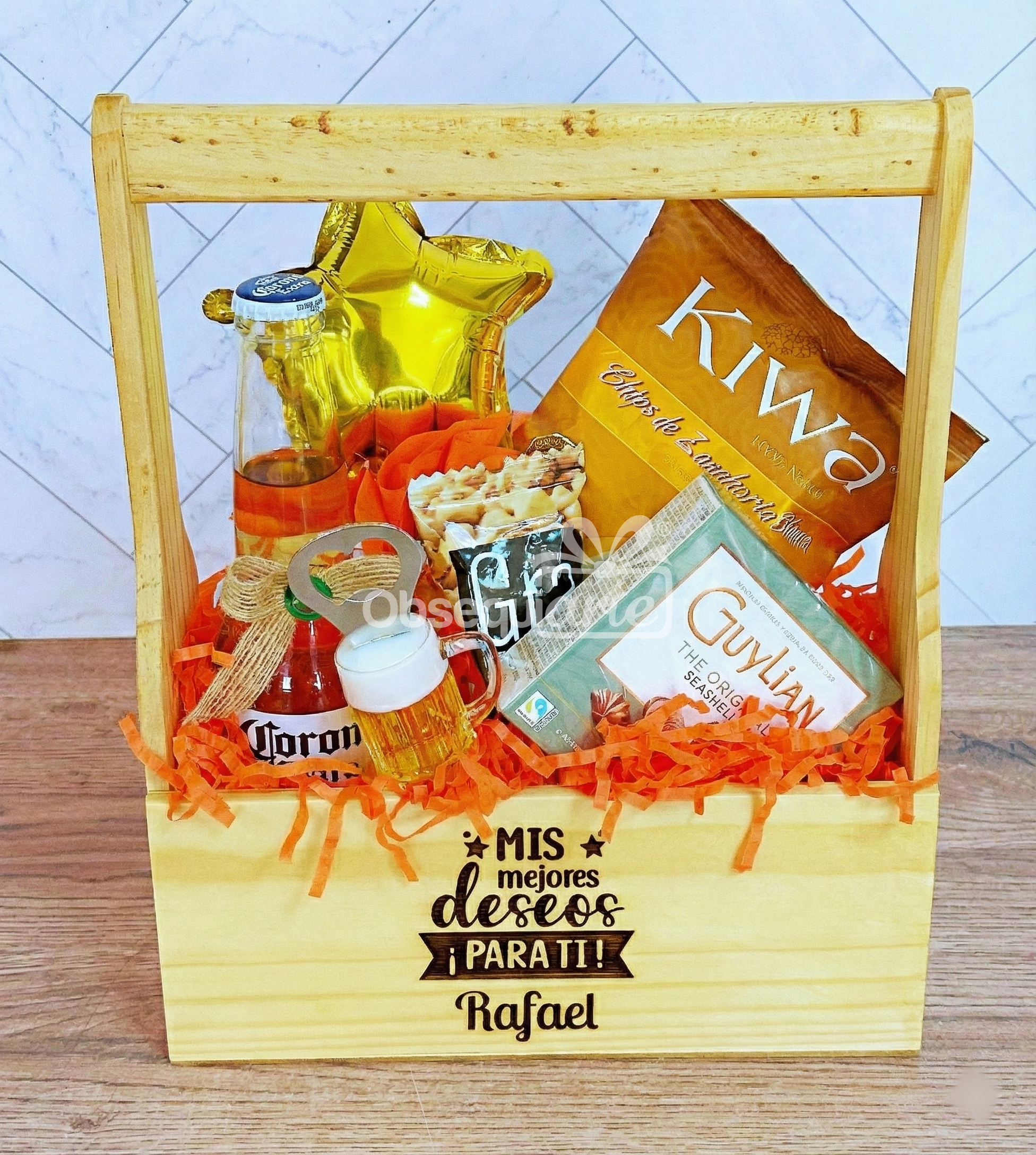 Un Regalo Jaba Personal con el mensaje "Mis mejores deseos para ti Rafael" incluye aperitivos, bombones, una mini botella de cerveza y un globo con una estrella dorada, bellamente expuestos en papel picado naranja.