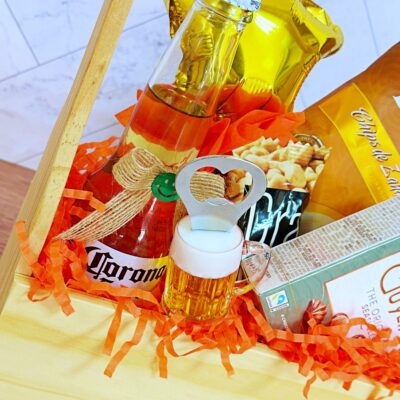 El Regalo Jaba Personal incluye una caja de madera con una cerveza Corona, un globo con una estrella dorada, patatas fritas, bombones, un pequeño abridor de jarras de cerveza y papel picado naranja para decorar.