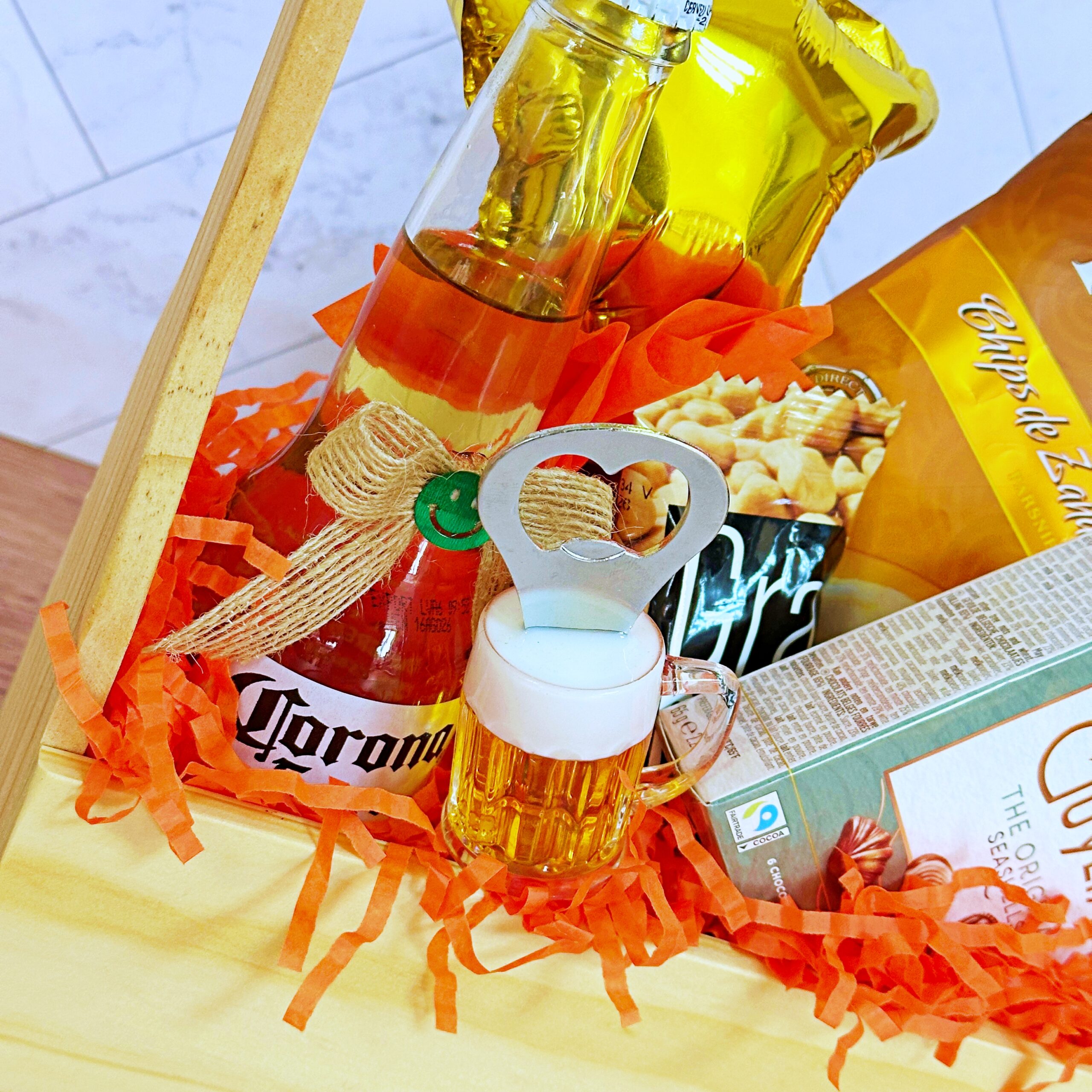 El Regalo Jaba Personal incluye una caja de madera con una cerveza Corona, un globo con una estrella dorada, patatas fritas, bombones, un pequeño abridor de jarras de cerveza y papel picado naranja para decorar.