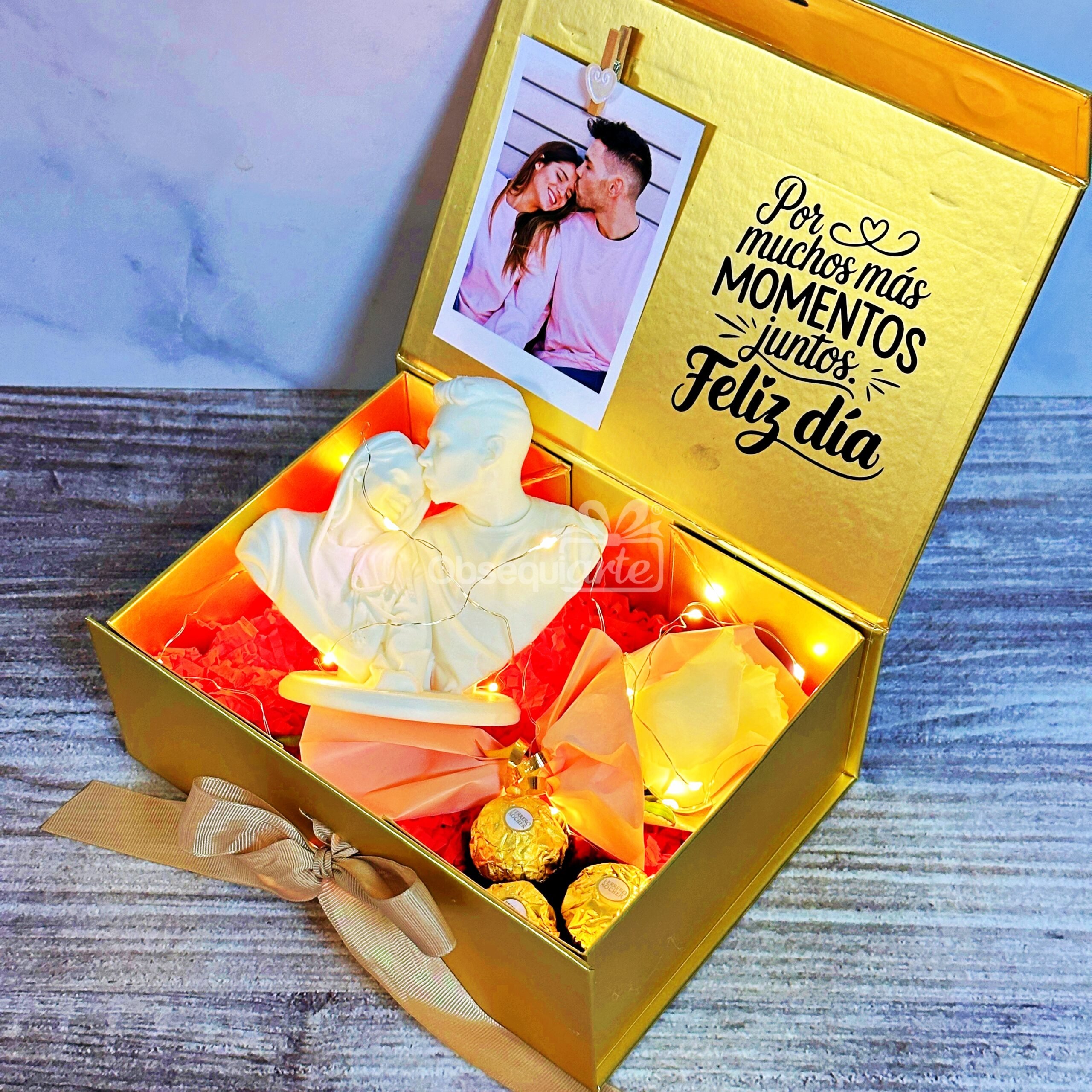 La caja de regalo Regalo Amor Eterno incluye luces de hadas, bombones, artículos decorativos, una foto de la pareja y el texto "Por muchos más momentos juntos. Feliz día" impreso en la tapa interior.