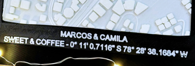 Primer plano de una placa que muestra un mapa, con el texto "MARCOS & CAMILA SWEET & COFFEE - 0° 11' 0.7116" S 78° 28' 38.1684" O" debajo.