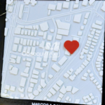 Un mapa 3D blanco con un corazón rojo que marca una ubicación específica cerca del centro, rodeado de varios edificios y carreteras.