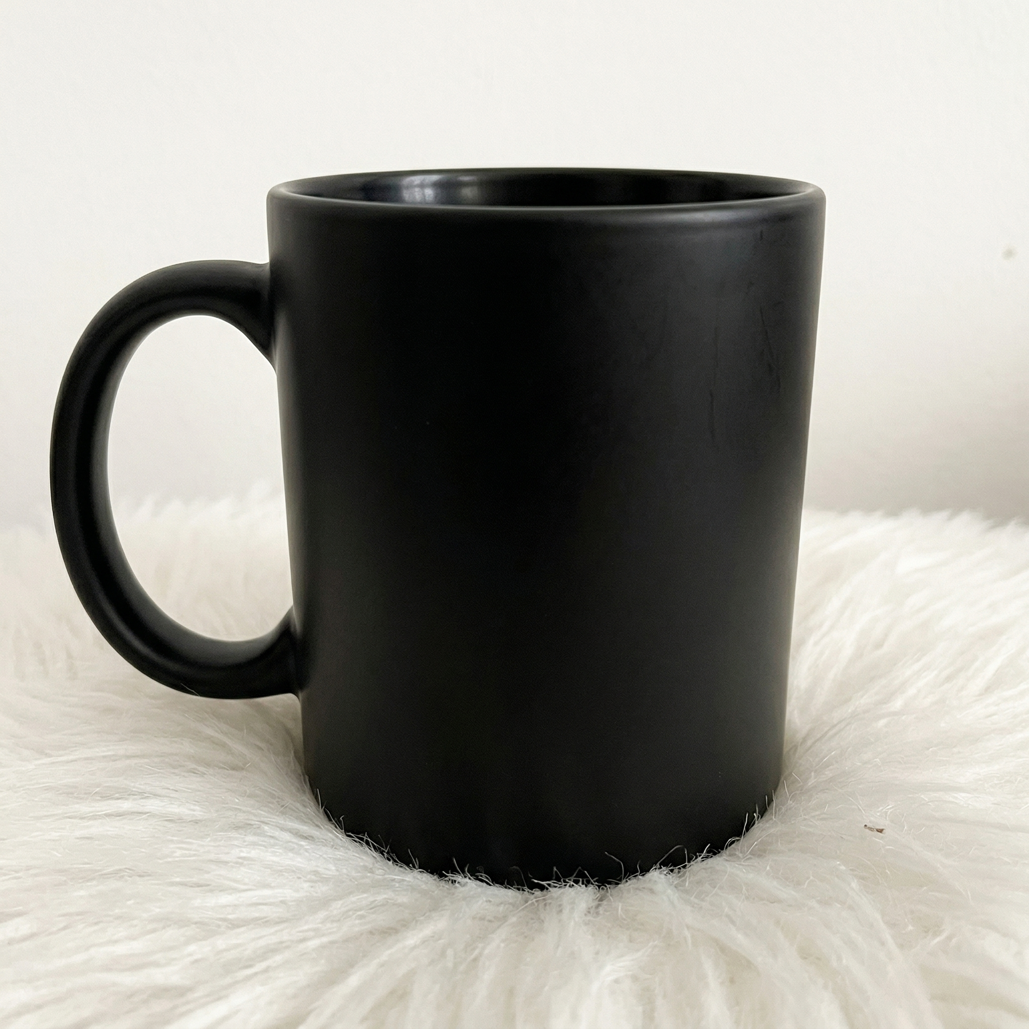 Una sencilla taza de cerámica negra descansa sobre una esponjosa superficie blanca sobre un fondo neutro, lo que la convierte en un Regalo Taza Mágica ideal para cualquier ocasión.
