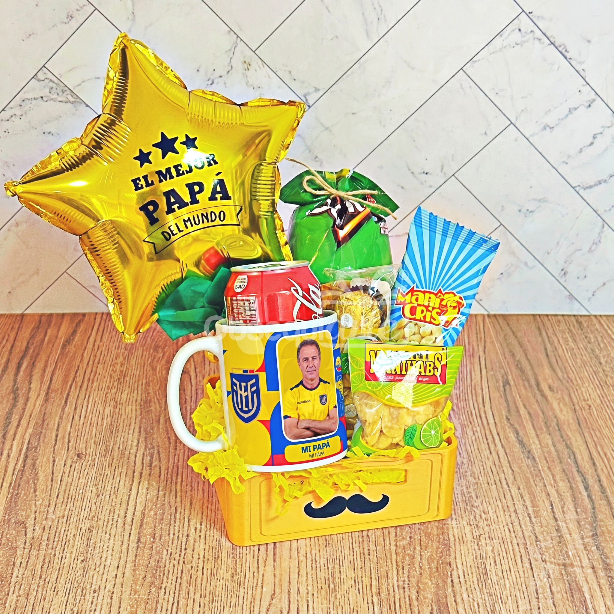 El «Regalo Papá Mundialista» es una caja de regalo amarilla con un dibujo de un bigote, aperitivos, una taza, una lata de Coca-Cola, un globo con forma de estrella que dice «El mejor papá del mundo» y un envoltorio decorativo; es un regalo ideal para papá, perfecto para colocar sobre una superficie de madera.