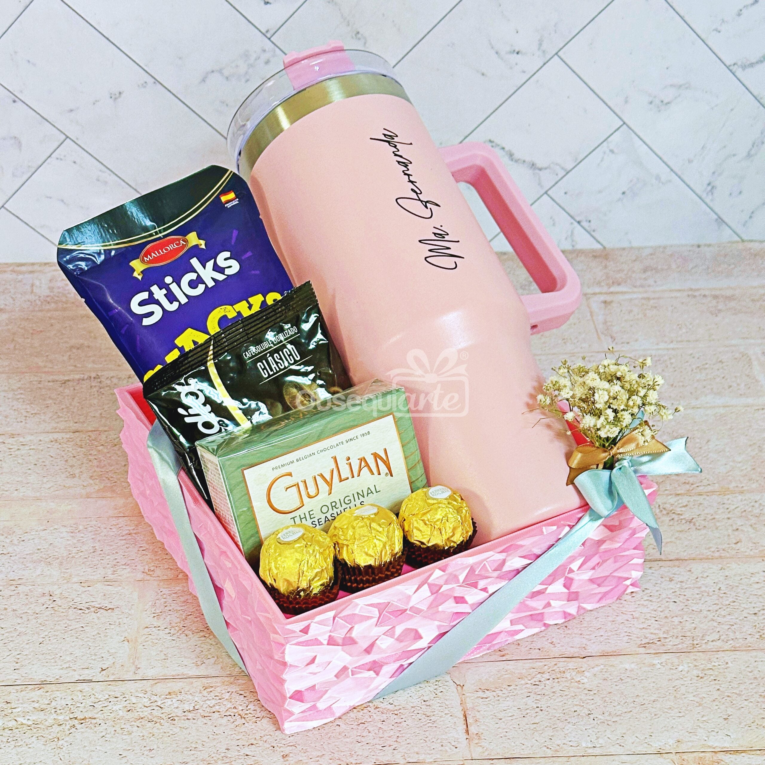 La caja Regalo Prestige (copia) es una cesta de regalo de color rosa que incluye un vaso rosa, chocolate Guylian, bombones Ferrero Rocher, barritas de aperitivo y un pequeño ramo de flores secas.